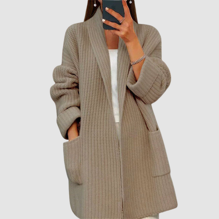 Close-up of a brown knitted cardigan worn by a person taking a mirror selfie against a neutral background.