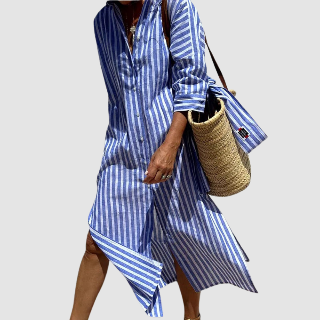 Woman in a blue striped summer dress with button details, carrying a straw bag, against a studio backdrop.