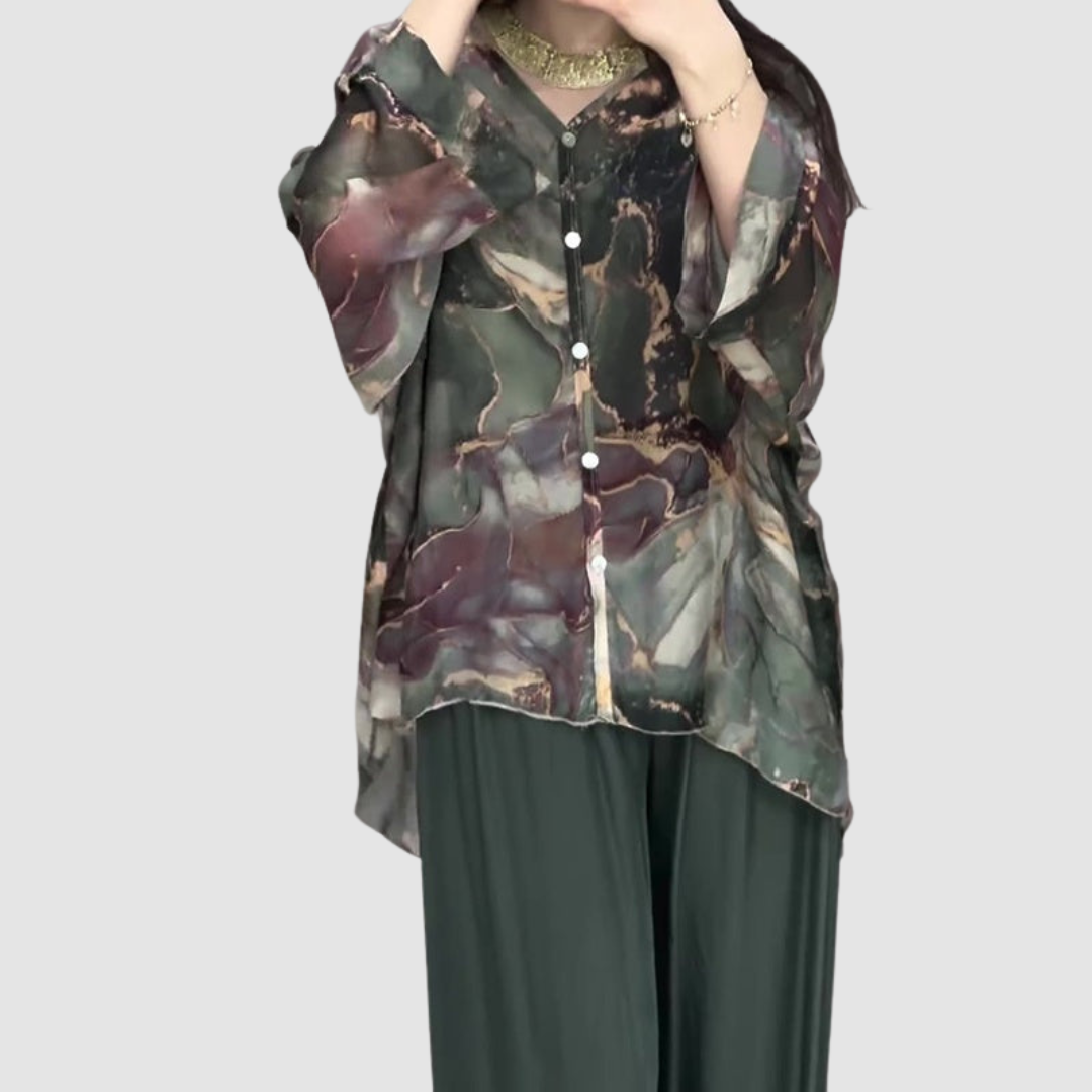 Model in elegant printed two-piece set, highlighting button-up top and relaxed pants against a bright plain background.