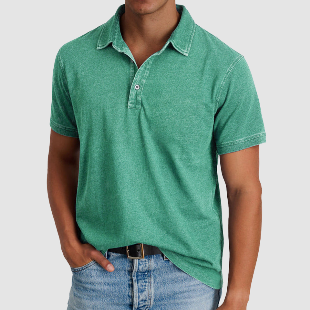 Model showcasing a green classic collared polo with short sleeves and a buttoned placket, paired with light blue jeans in a studio.