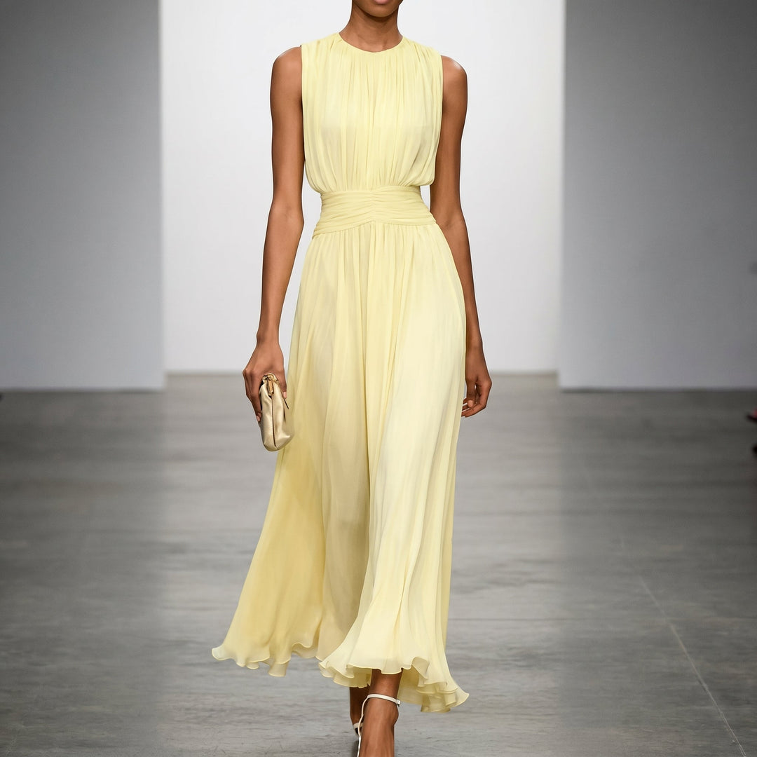 Flowing yellow elegant dress in indoor studio setting, model holding a clutch.