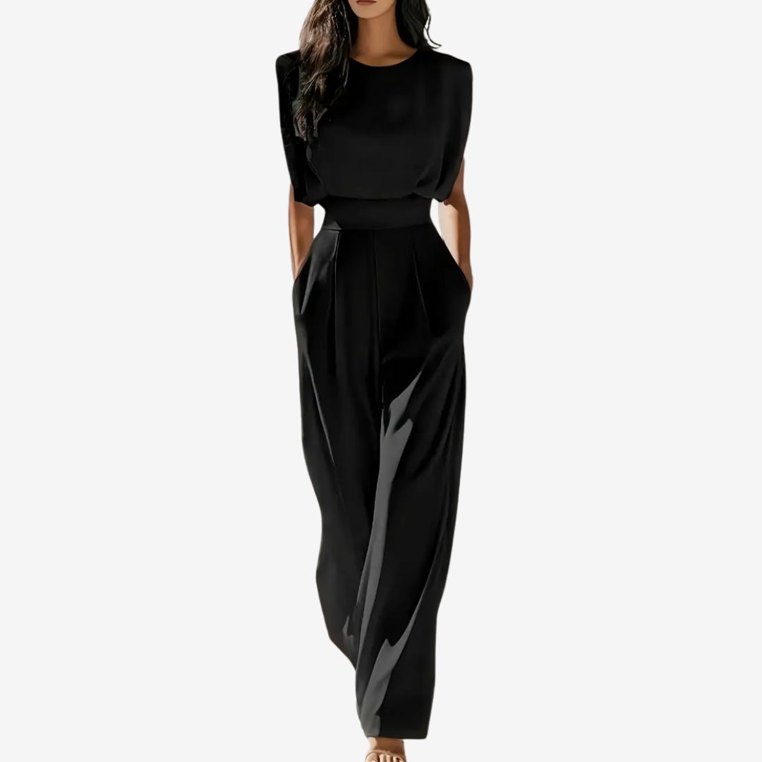 Black sleeveless jumpsuit with wide legs, worn by model in studio setting, hands in pockets.