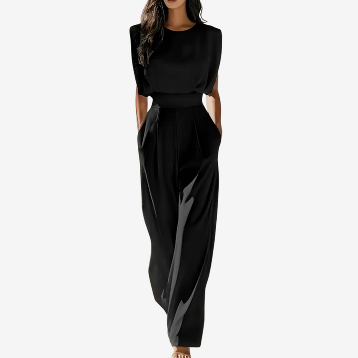 Black sleeveless jumpsuit with wide legs, worn by model in studio setting, hands in pockets.