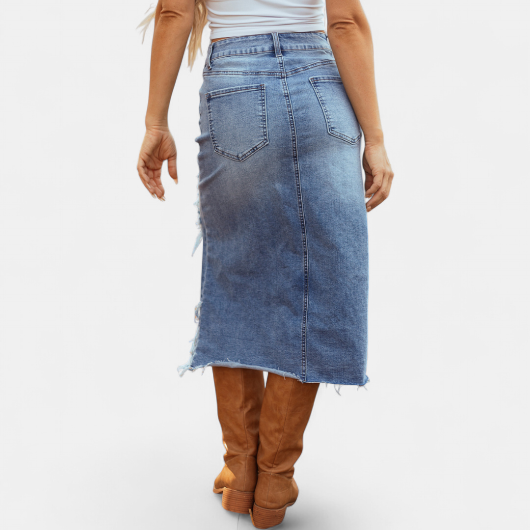 Back view of a high-waist denim maxi skirt with two pockets paired with brown boots in a studio setting.