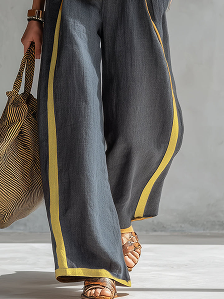 Close-up of dark wide-leg pants with yellow stripe, held by model with a striped bag, in a studio setting.