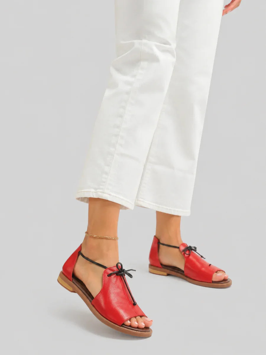 Red leather sandals on feet, worn with white pants, gray background.