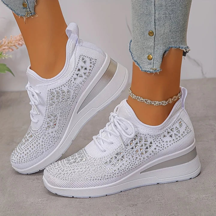 White orthopedic sneakers with subtle shimmer, styled with jeans, displayed on a flat indoor surface.