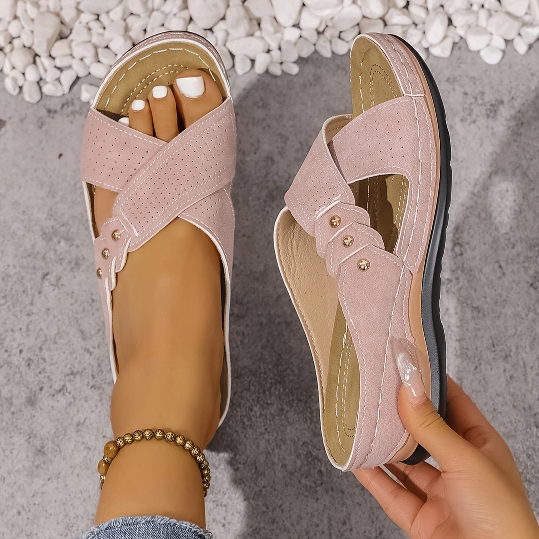 Pink orthopedic wedge sandals held in hand, displayed on a textured surface with white stones.