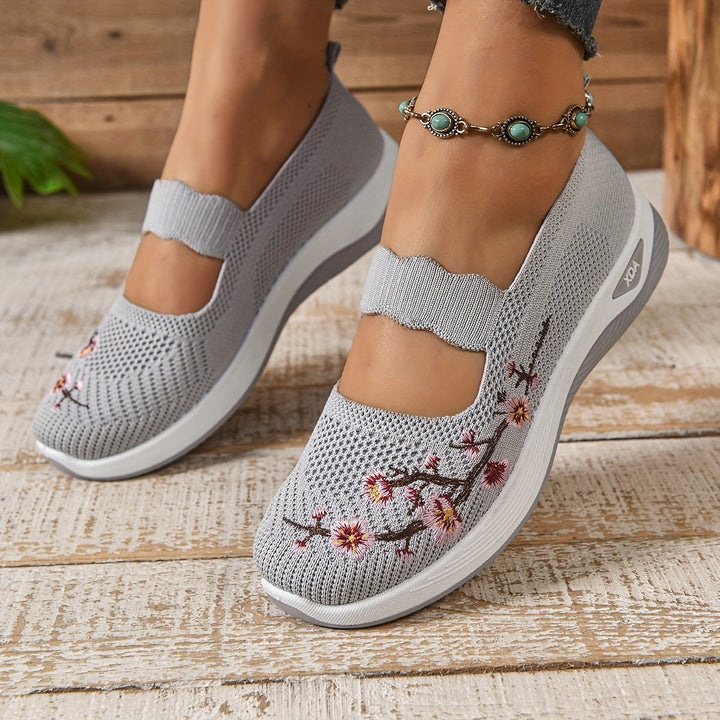 Gray orthopedic shoes with flower embroidery, paired with anklet, on a rustic wooden floor.