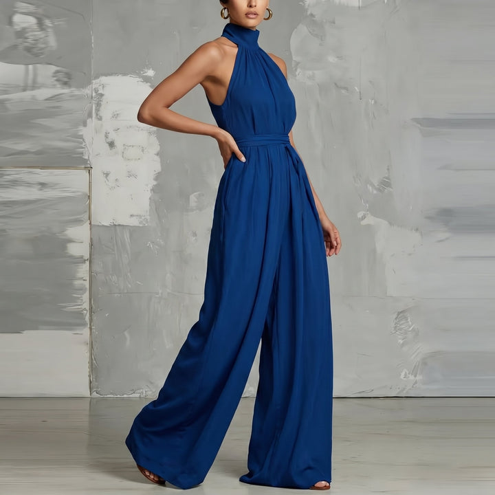 Modern blue halter-neck jumpsuit with flowing wide legs in a stylish studio setting.