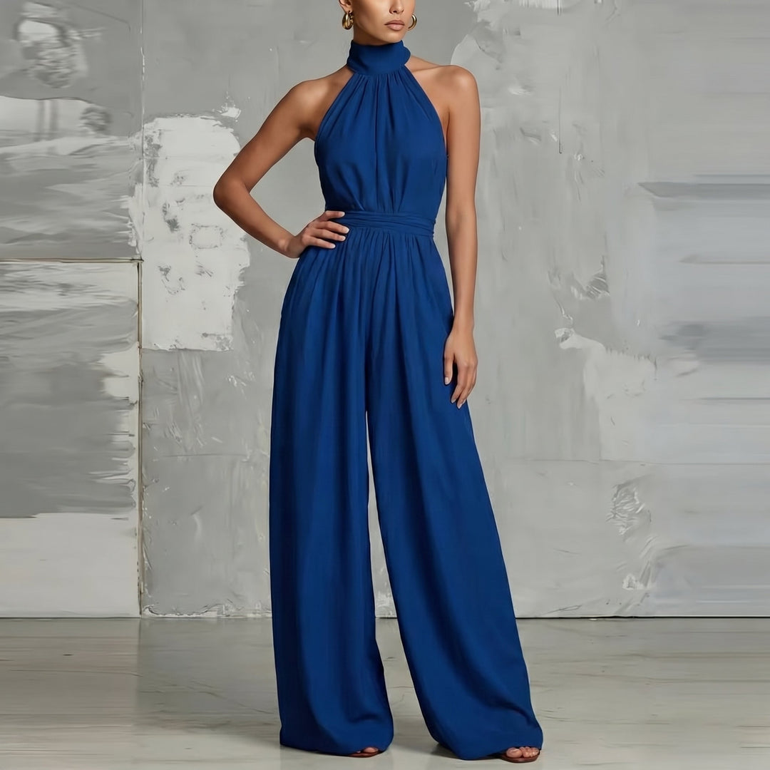 Blue halter-neck jumpsuit with wide legs, posed elegantly in a contemporary studio.