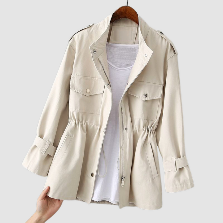 Light beige jacket with a front button closure, drawstring waist, and flap pockets, hanging on a wooden hanger with white background.