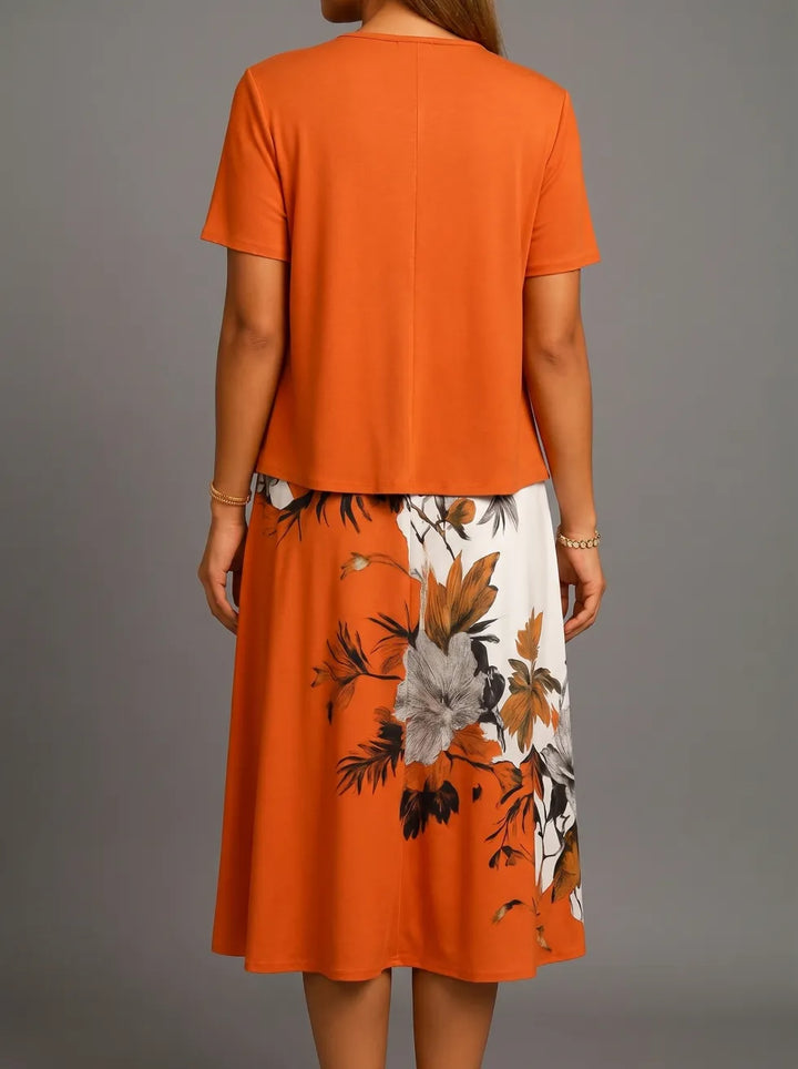 Back view of orange midi dress with floral accents and short sleeves, displayed in a studio setting.