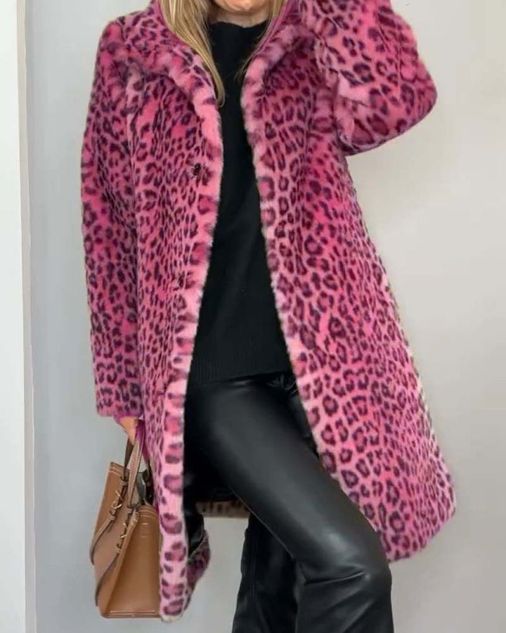 Woman sporting a pink leopard print coat, wearing a black outfit with a brown handbag in a minimalist indoor space.