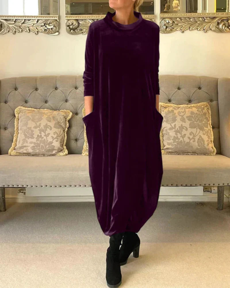 Purple flowing suede dress with pockets, worn indoors in front of a tufted sofa with patterned pillows.