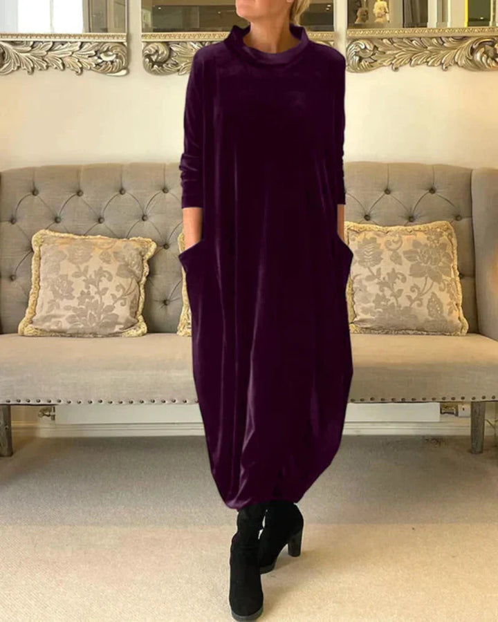 Purple flowing suede dress with pockets, worn indoors in front of a tufted sofa with patterned pillows.