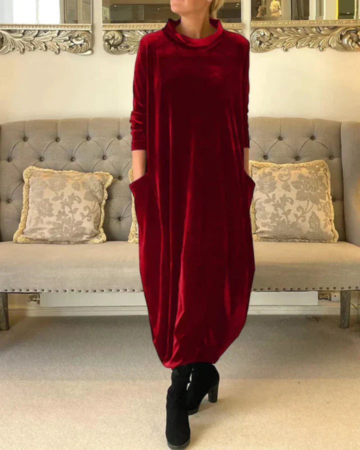 Red flowing suede dress with pockets, modeled indoors. Background features a beige tufted sofa with pillows.