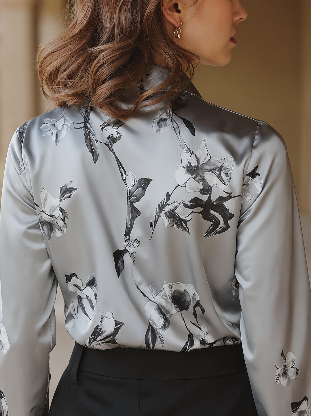 Rear view of grey satin blouse with floral design, model standing indoors with subtle background.