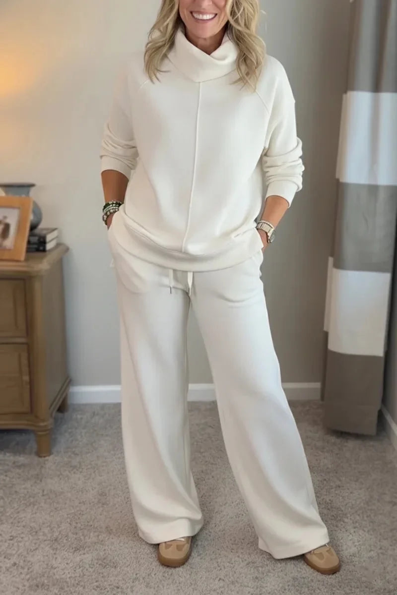 Woman in a white comfortable set with long sleeves and wide-leg pants, standing in a cozy, carpeted room.