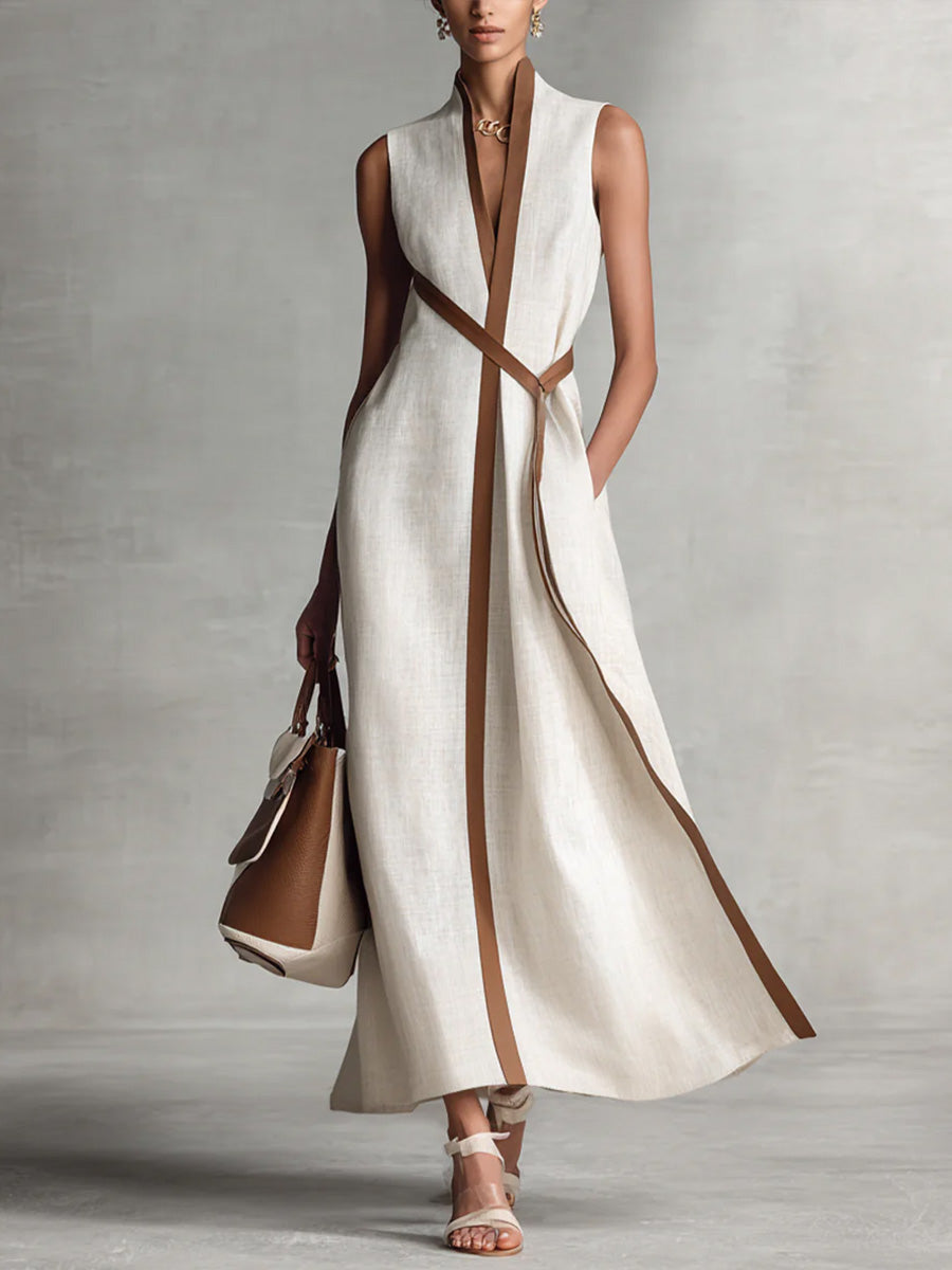 Elegant sleeveless beige maxi dress with brown trim, styled with a handbag and sandals in a studio setting.