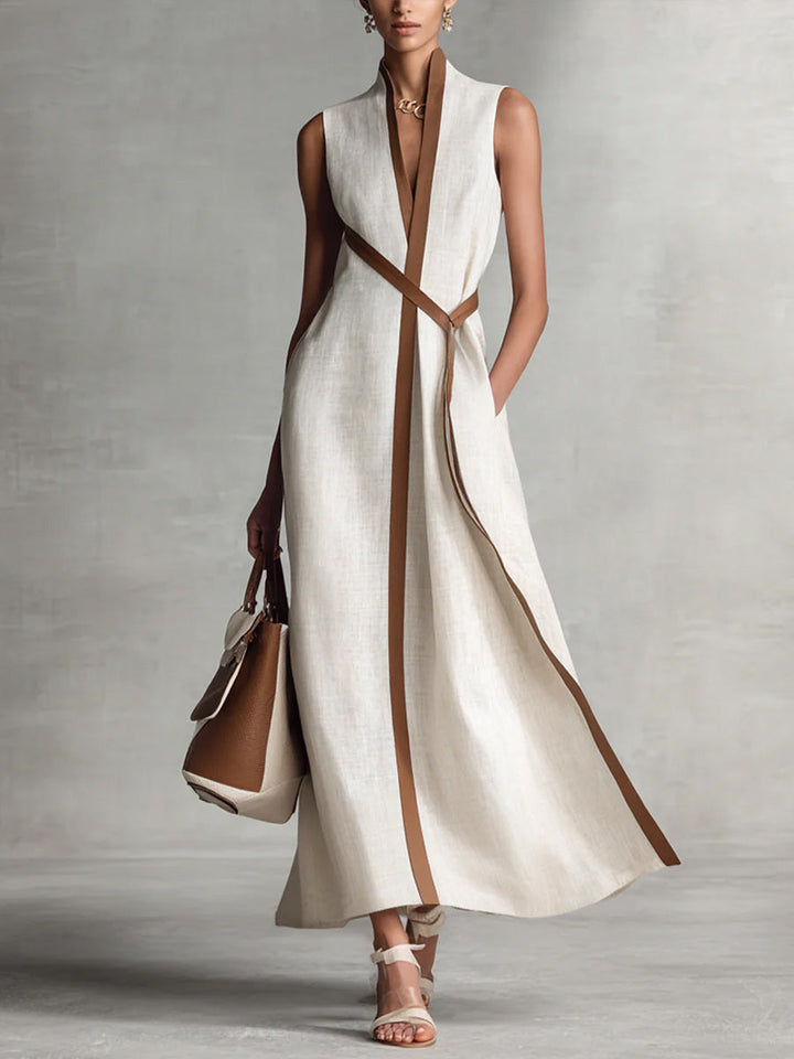 Elegant sleeveless beige maxi dress with brown trim, styled with a handbag and sandals in a studio setting.