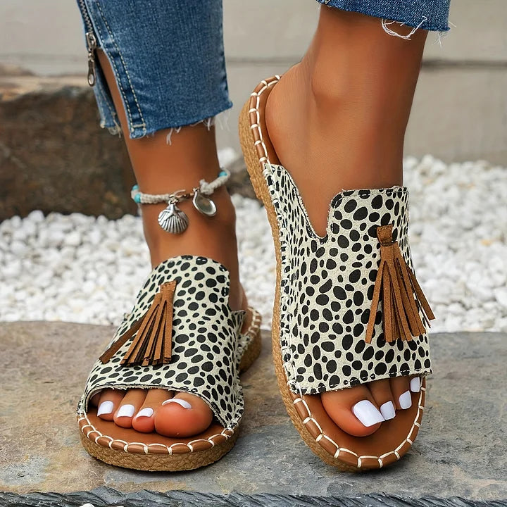 Polka dot orthopedic sandals with tassels worn outdoors on stone path.