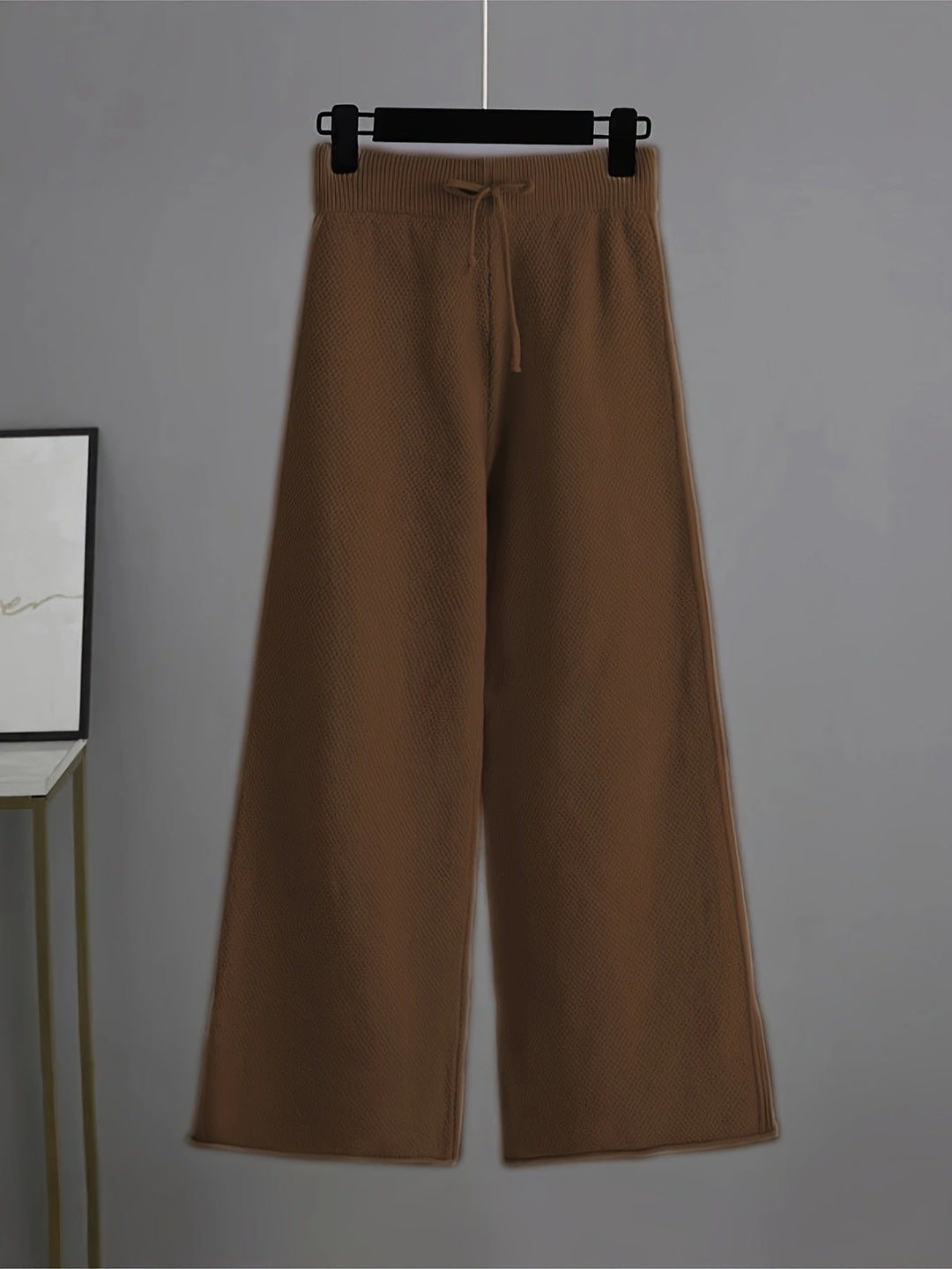 Brown knit pants with a drawstring and relaxed fit on a hanger, gray background.