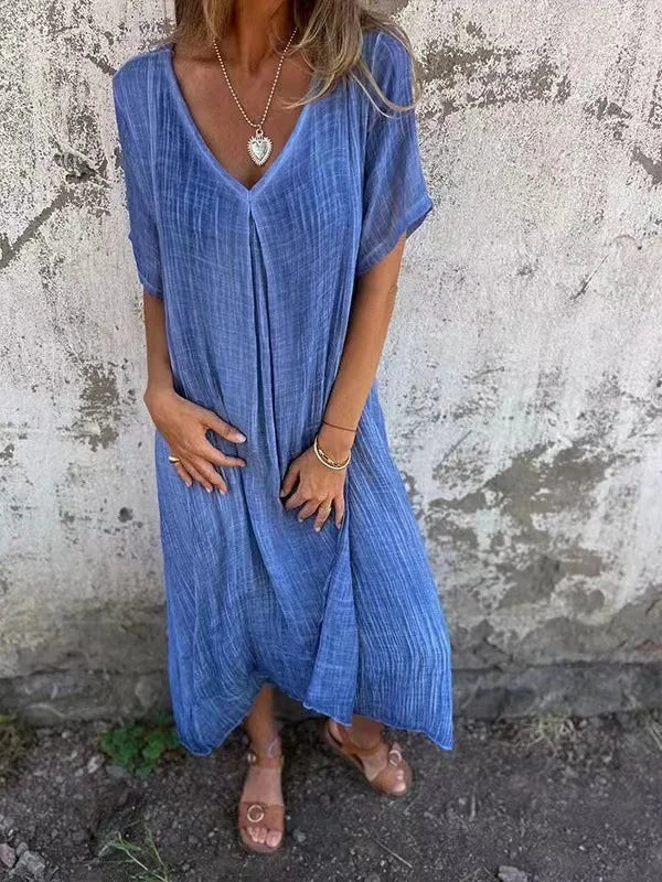 Blue V-neck dress with short sleeves, worn by a person in front of a textured wall.