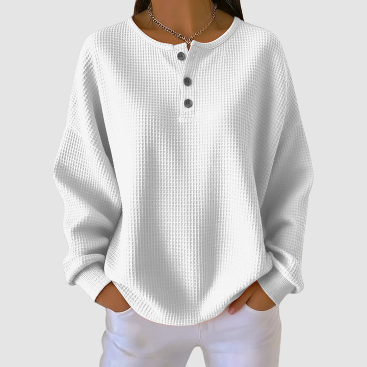 White relaxed sweater with buttoned neckline and textured fabric, worn with white pants in a studio setting.