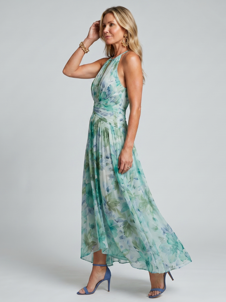 Side view of woman wearing green floral maxi dress and blue heels in studio setting.