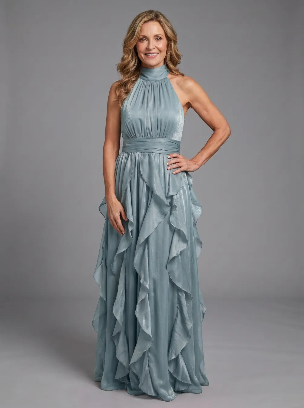 Model wearing a teal high neck maxi dress with ruffle layers, posing in a studio with a gray background.