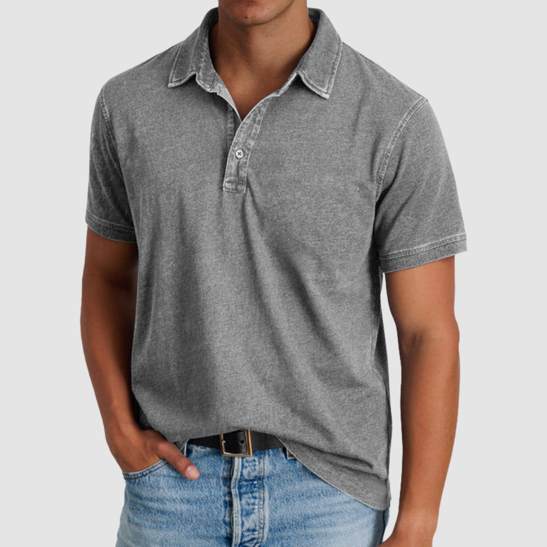 Model in a grey classic collared polo, short sleeves, buttoned placket, light jeans, studio background.