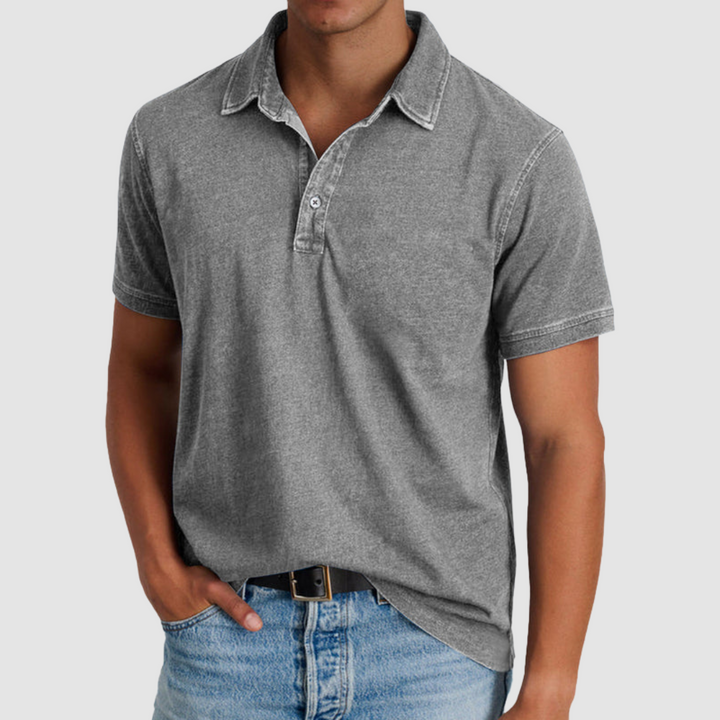 Model in a grey classic collared polo, short sleeves, buttoned placket, light jeans, studio background.