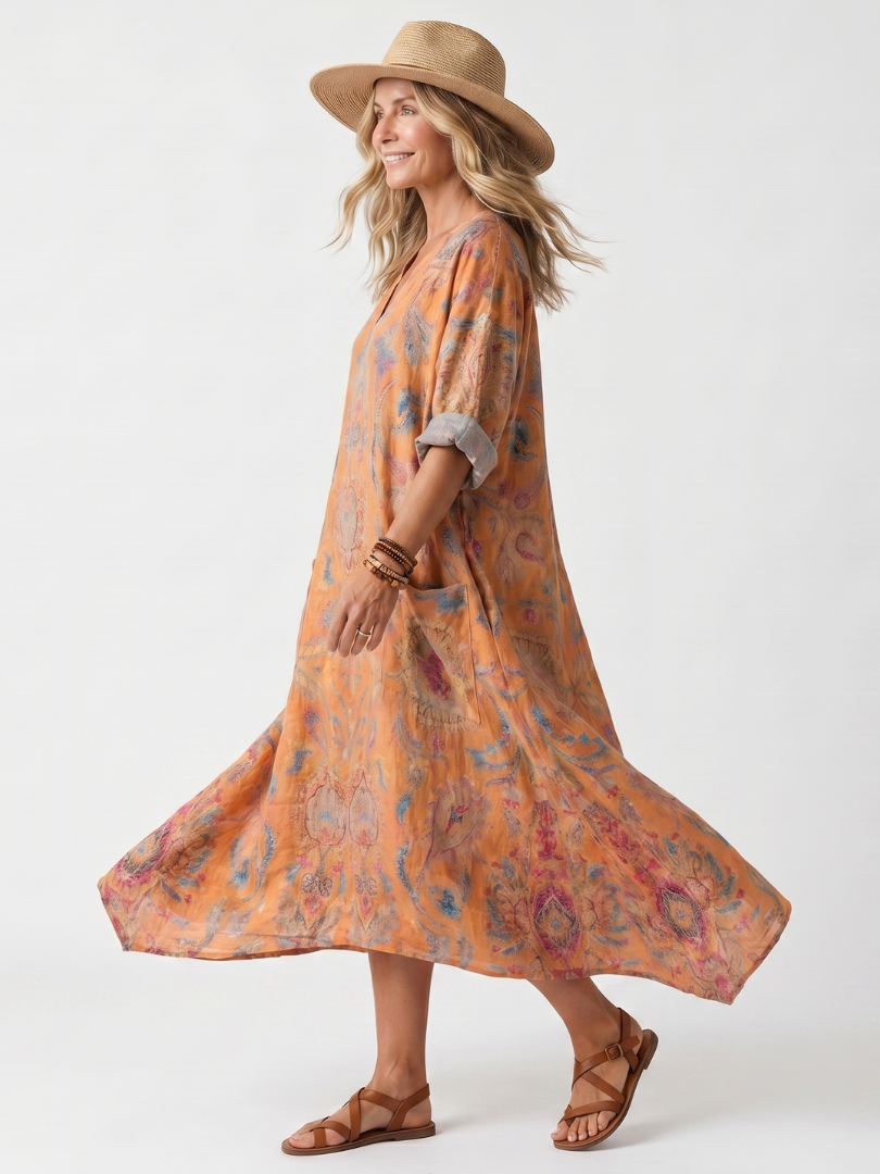 Side view of orange printed oversized midi dress with pockets, notch neck, and cuffed sleeves, modeled with a hat in a studio.