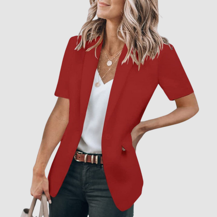 Red short-sleeve blazer worn by person with wavy hair, white top, and jeans; holding a beige handbag against a plain background.