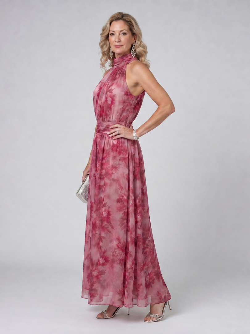 Woman posing side view in pink floral halter neck midi dress with silver clutch in a studio setting.