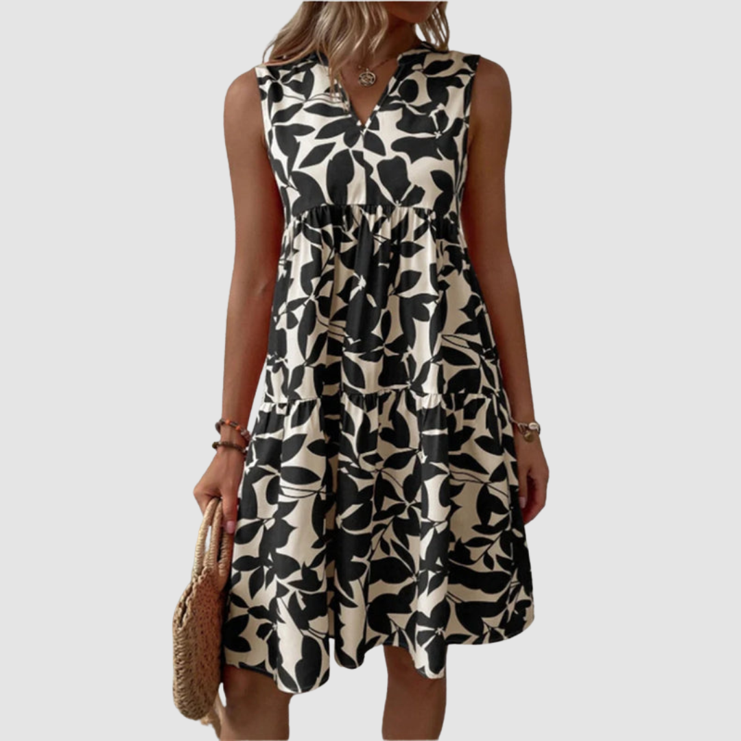 Model wearing a sleeveless black and white floral print flowy dress, holding a woven bag, against a plain background.