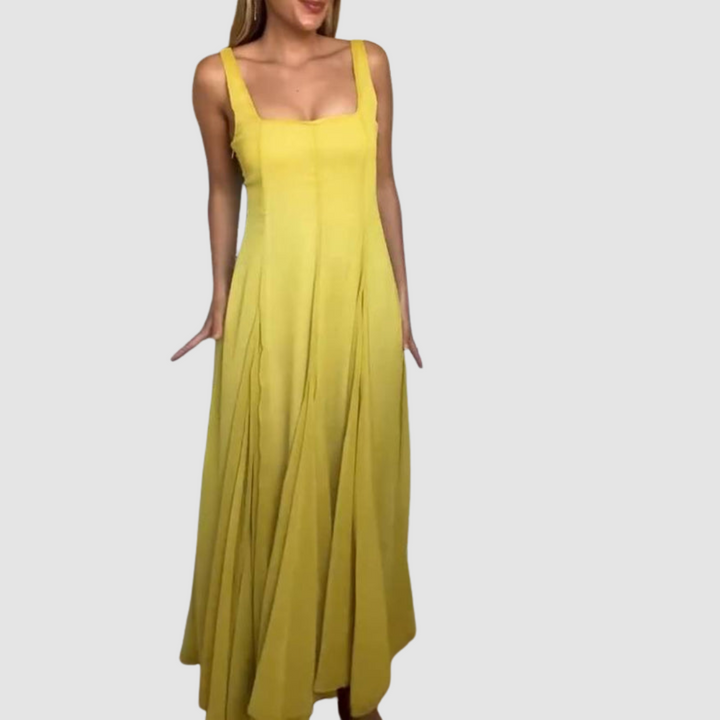 Yellow maxi dress with broad straps and flowing skirt, model standing upright in a studio setting.