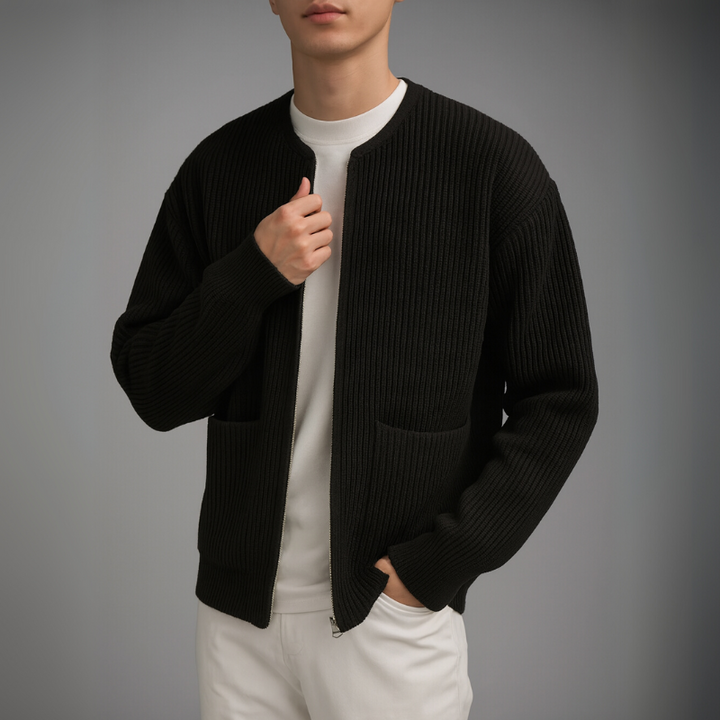 Model in a black knit zip cardigan over a white shirt and pants in a studio.