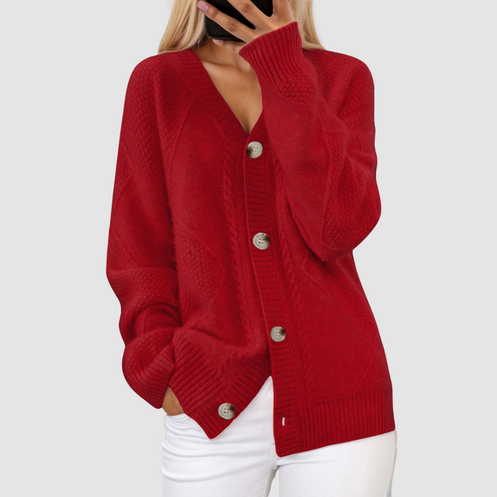 Red knitted V-neck cardigan with button closure, worn by person with hand in pocket, set against a light gray background.