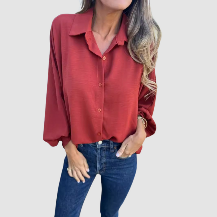Model wearing a red oversized blouse with buttons, blue jeans, hand in pocket, gray background.