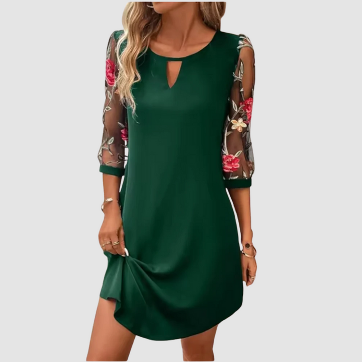 Green summer dress with sheer floral print sleeves, displayed indoors on a neutral background.