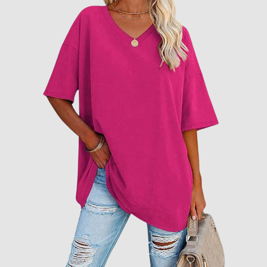 Woman in a pink V-neck T-shirt with distressed jeans, carrying a beige bag, studio setting.
