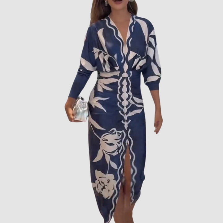 Navy V-neck dress with striking white designs, long sleeves, and a front slit. Model holding a silver clutch in a simple studio backdrop.