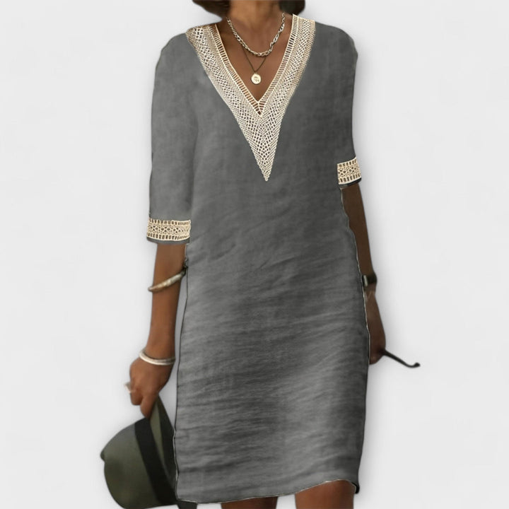Gray elegant dress with V-neck and lace trim, paired with silver jewelry on a simple backdrop.