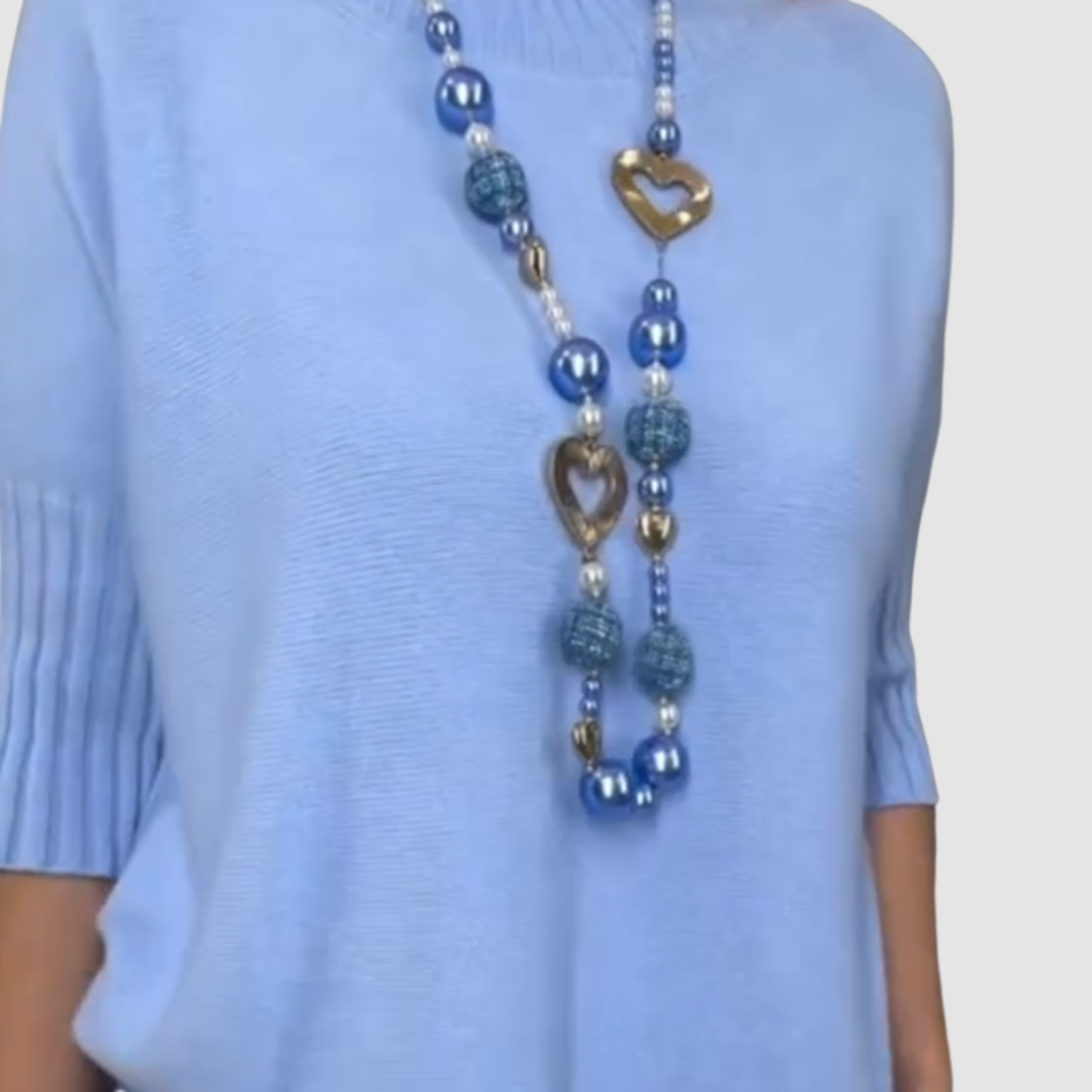 Close-up of light blue top from 2-piece set with heart-themed beaded necklace on plain background.