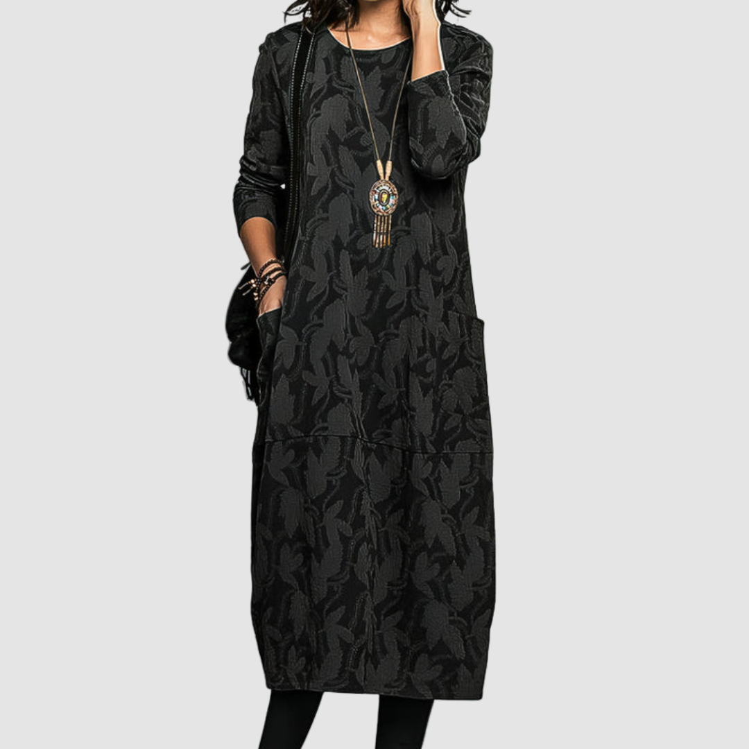 Model showcasing a classy black dress with subtle patterns, paired with a bold necklace, set against a clean background.