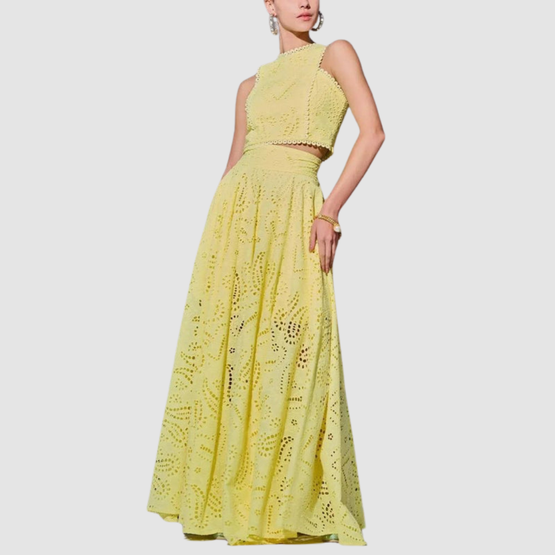 Woman in a yellow two-piece set featuring detailed cutout patterns, posing with arm on hip against a white background.