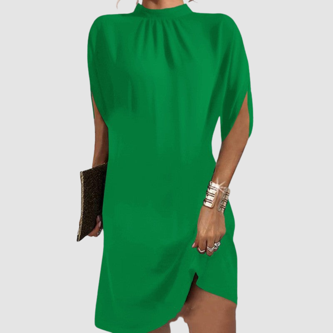 Green knee-length dress with a relaxed silhouette and high neckline, shown with gold bangles and clutch on a gray backdrop.