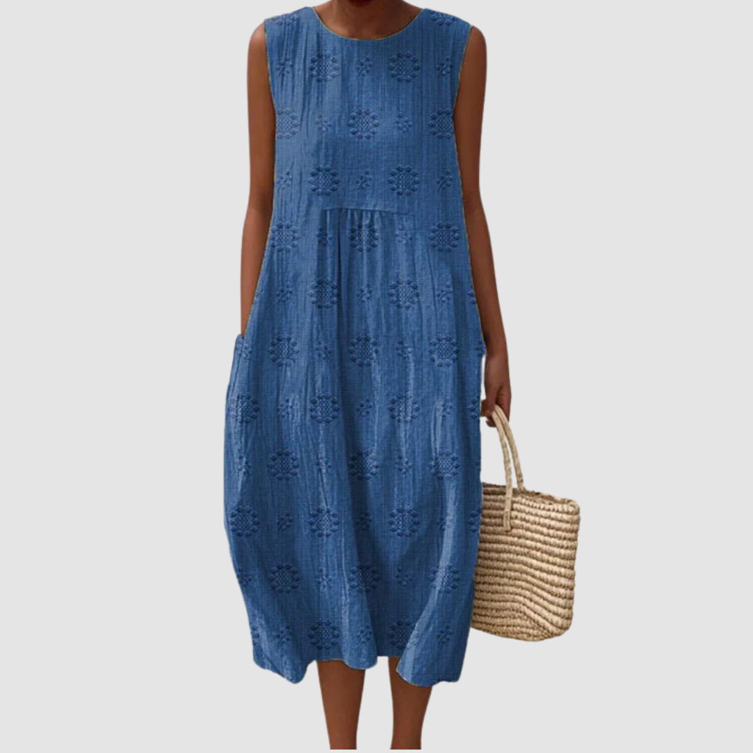 Blue sleeveless summer dress with floral patterns, model holding a woven basket, white background.